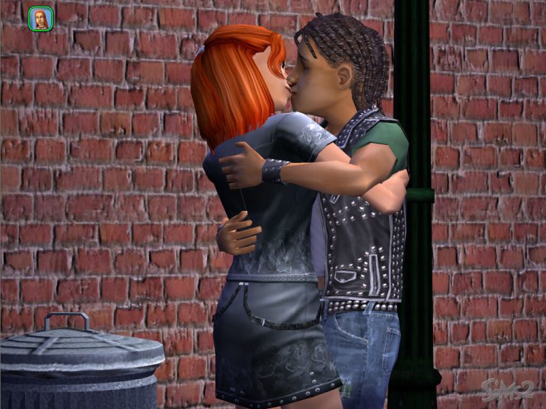 Screenshot of The Sims 2 showing two Sims kissing outdoors at night. They are standing on a sidewalk next to a dark green street lamp and a metal trash can, in front of a red brick wall. One Sim has bright orange hair and is wearing a dark studded outfit with a skirt. The other Sim has brown hair in dreadlocks and is wearing a black studded vest over a green t-shirt and jeans. The classic The Sims 2 logo is faintly visible in the bottom right corner.